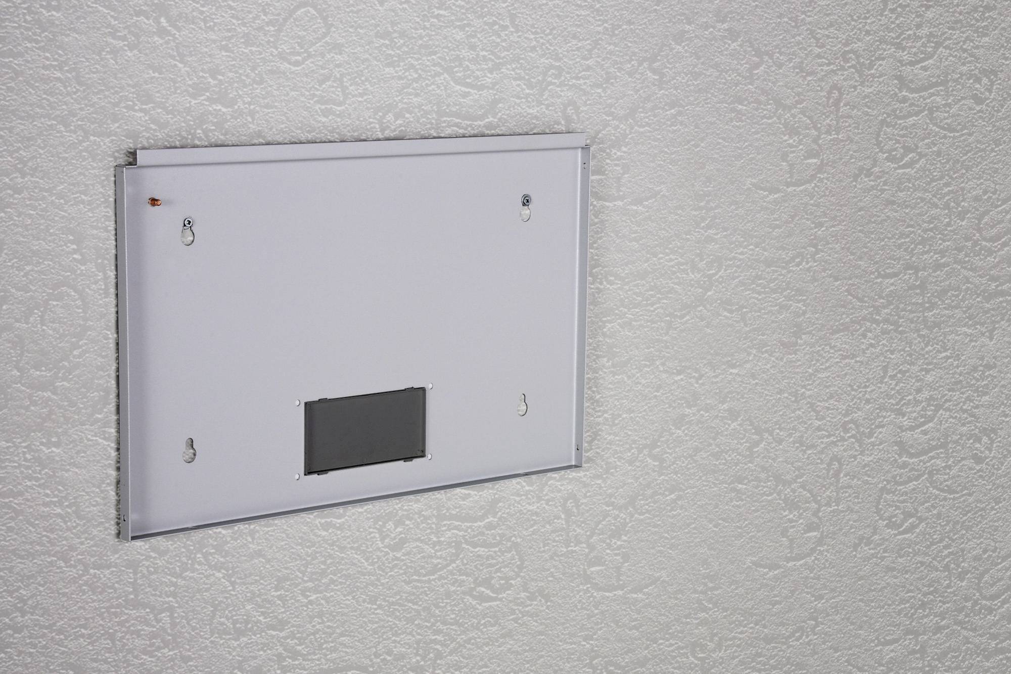 A white rectangular panel is mounted on a textured wall. It has a small black surface at the bottom centre.