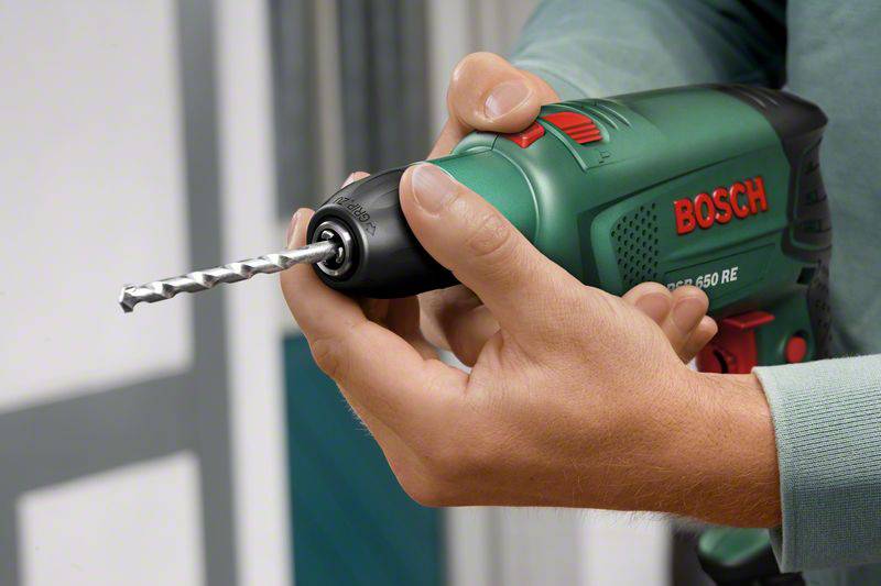A person is holding a green Bosch electric drill, ready to drill.