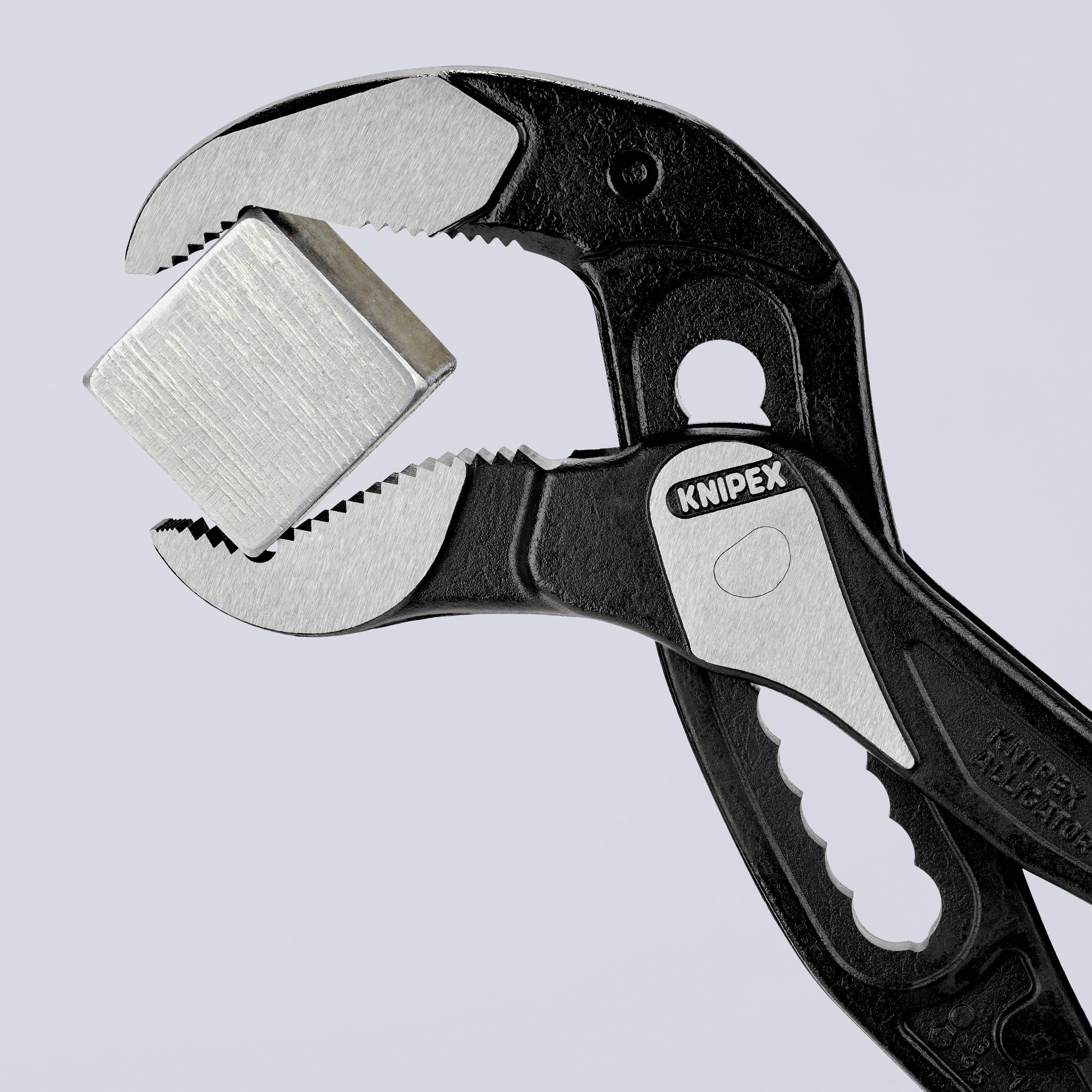 A black pair of pliers grips a silver metal cube.