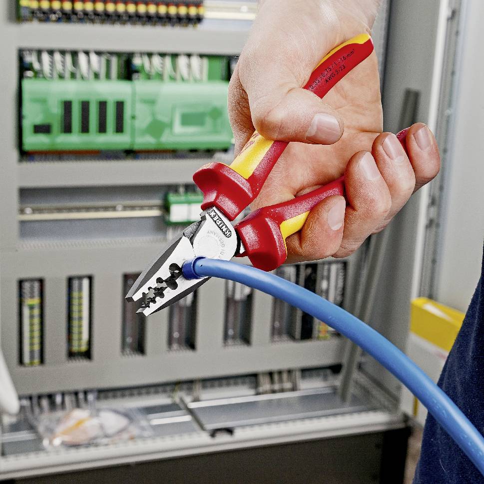 A hand is holding pliers cutting through a blue cable. In the background, an electrical cabinet with multiple components can be seen.
