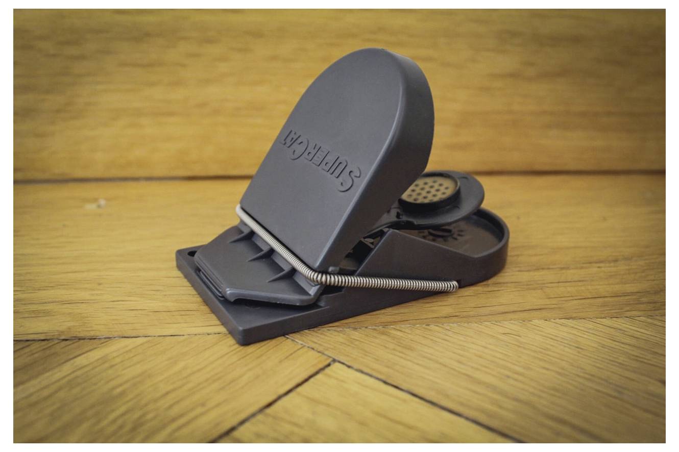 A black plastic mouse trap labeled 'Suffolk', set and ready to catch, placed on a wooden floor.
