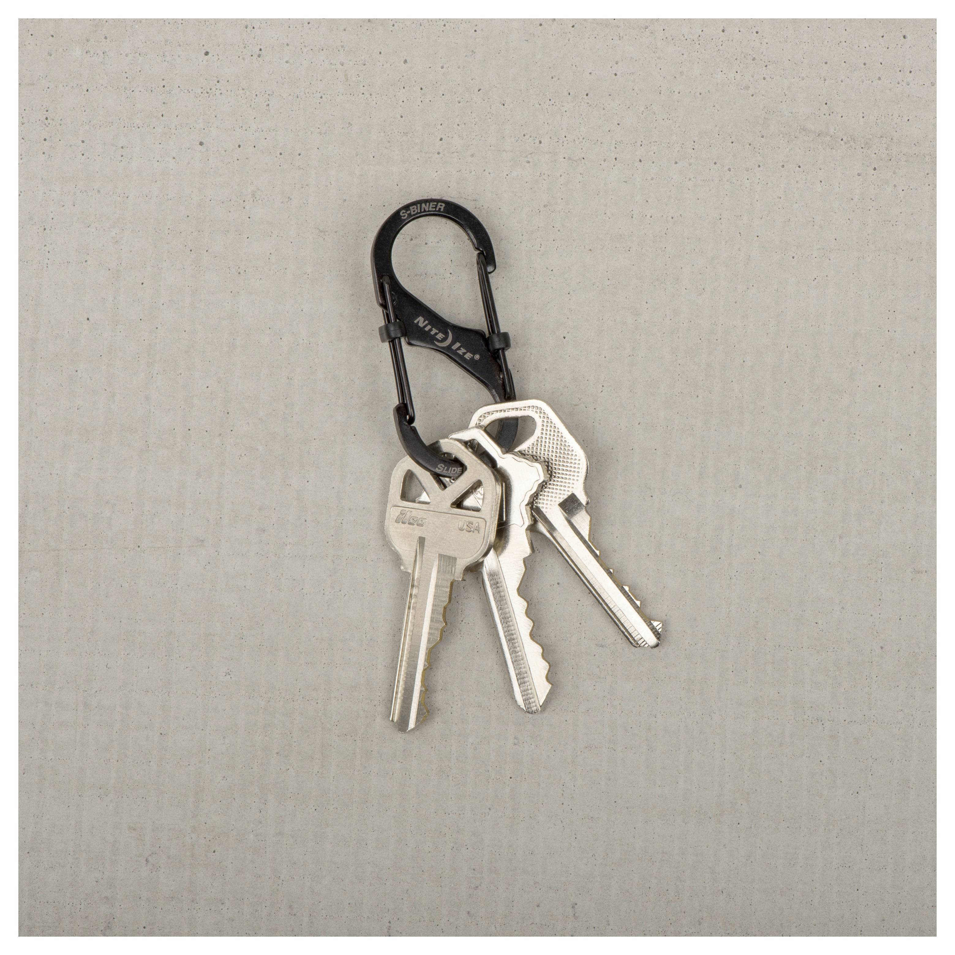 A carabiner keychain holds three silver keys, resting on a textured gray surface.