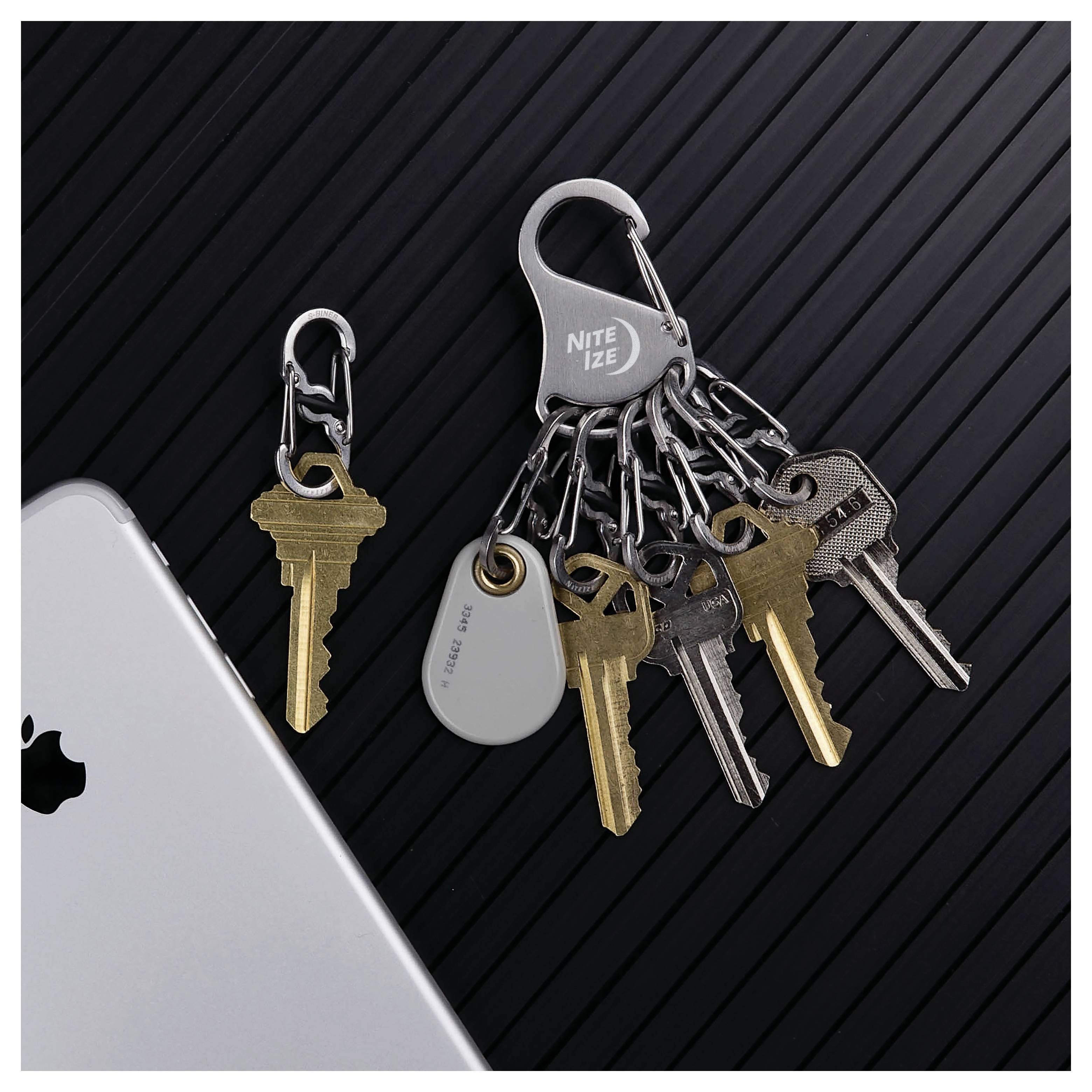 A set of six keys attached to a 'Nite Ize' key holder on a black textured background, next to a smartphone and a single loose key.