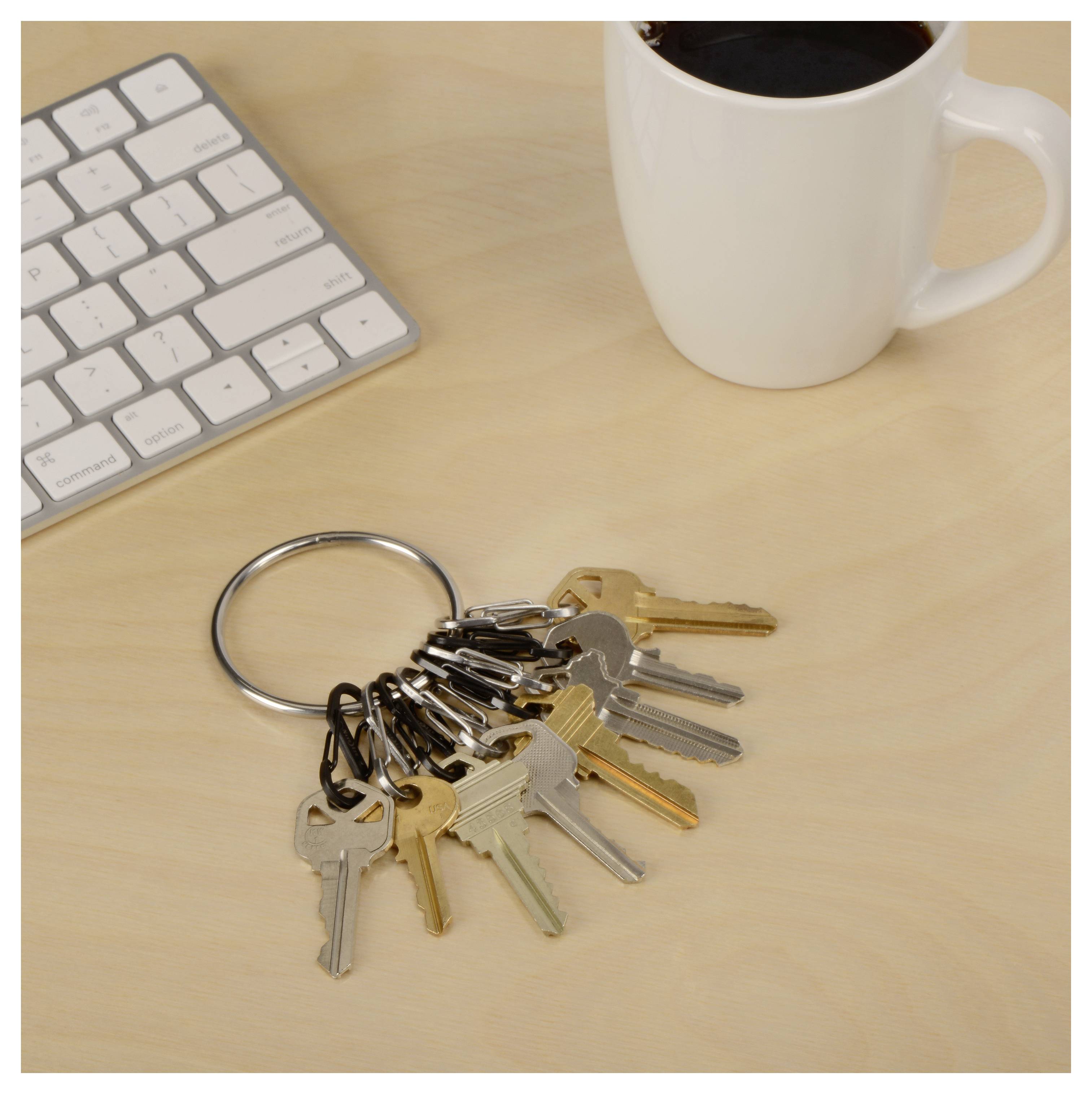 'A set of various keys on a keyring lies next to a keyboard and a white coffee mug on a wooden desk.'