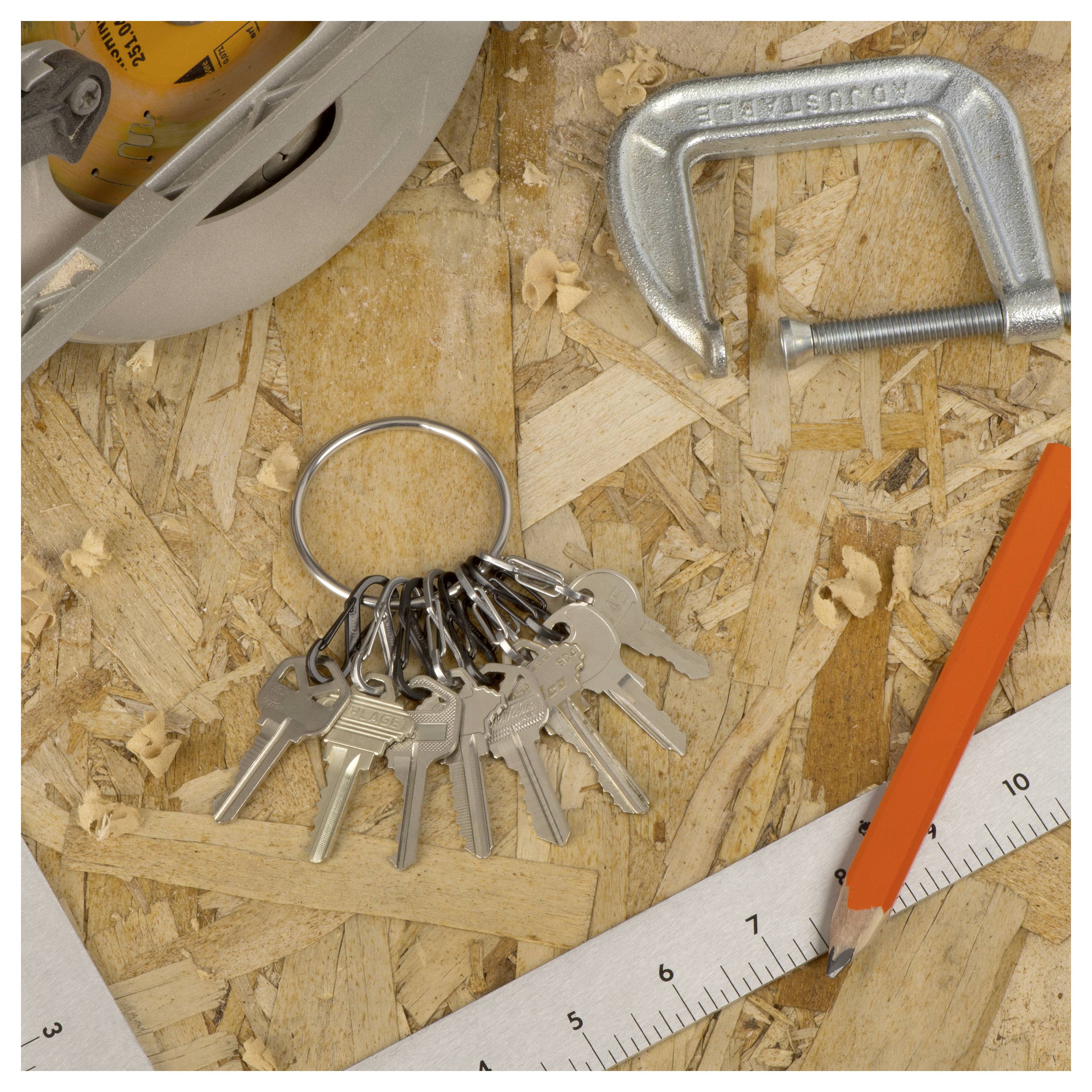 Keys on a ring rest on wood, surrounded by a metal clamp, a ruler, a pencil, and a circular saw blade.