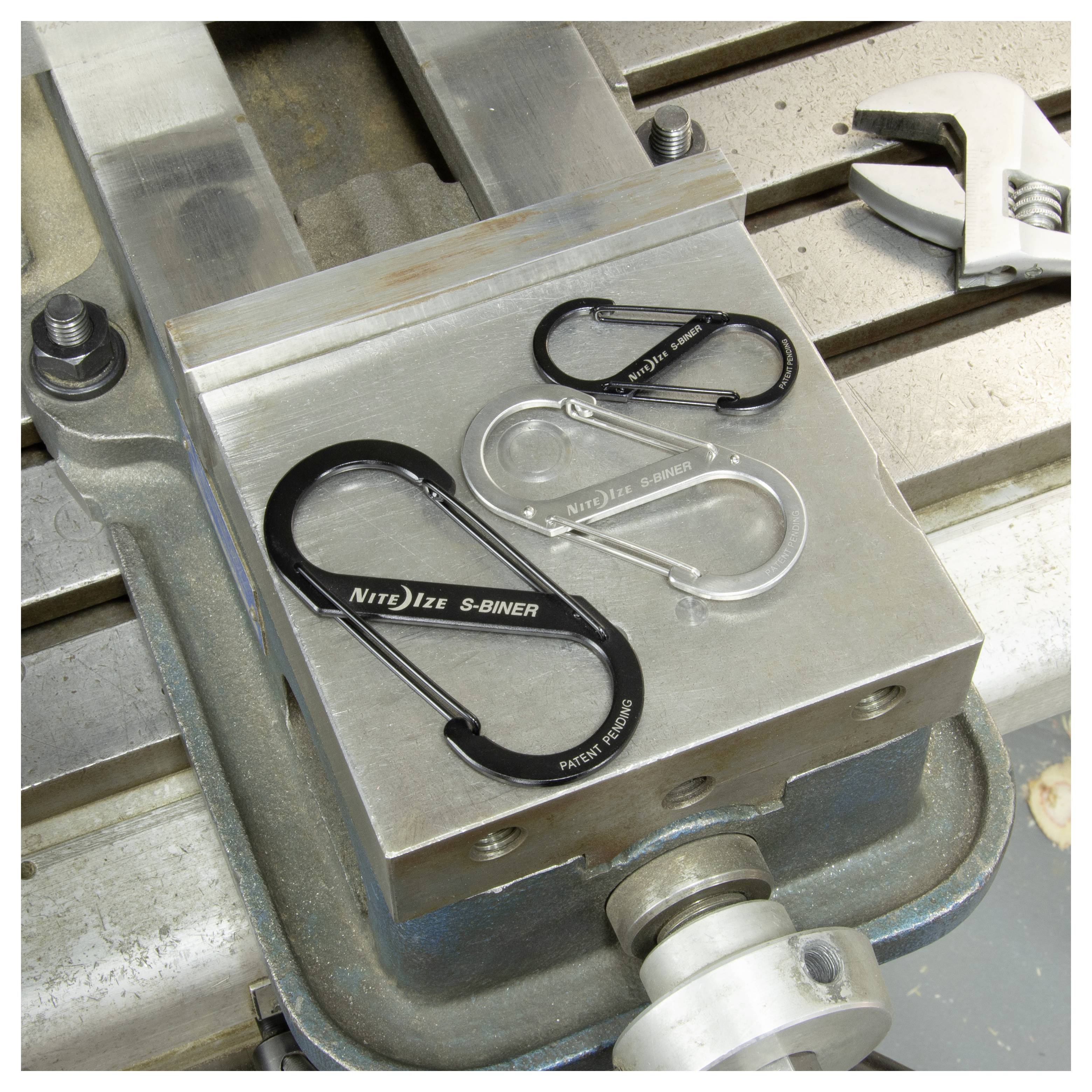 Three metallic carabiners of different sizes on a metal surface, with a wrench nearby, showcasing variety in tools.