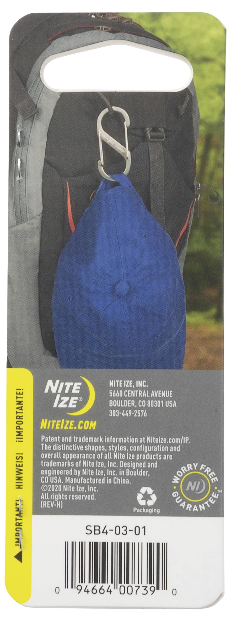 A black and gray backpack with a blue cap attached using a silver carabiner clip. Background shows a blurred outdoor setting.