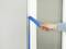 A hand is peeling masking tape from a window frame, possibly after painting.