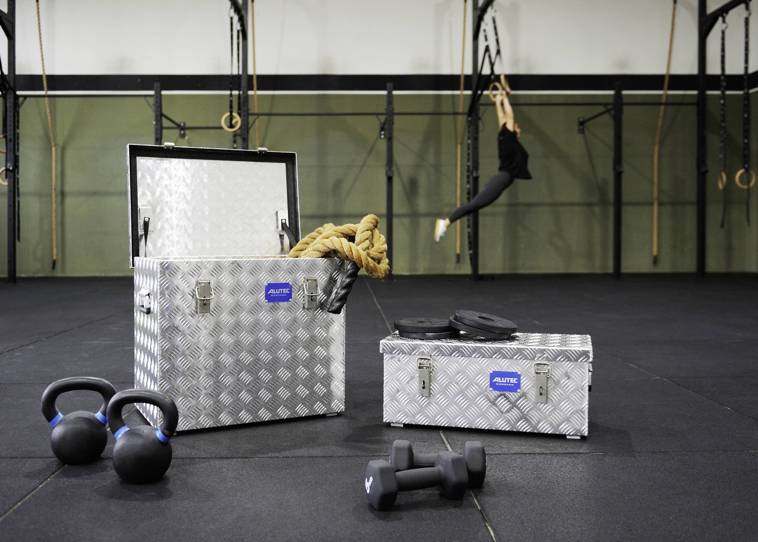 Kettlebells, dumbbells and ropes on a fitness studio floor with hanging rings and a person in motion in the background.