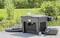 'Outdoor pond filter system placed on a wooden deck, surrounded by greenery, with a black pump and coiled hose.'
