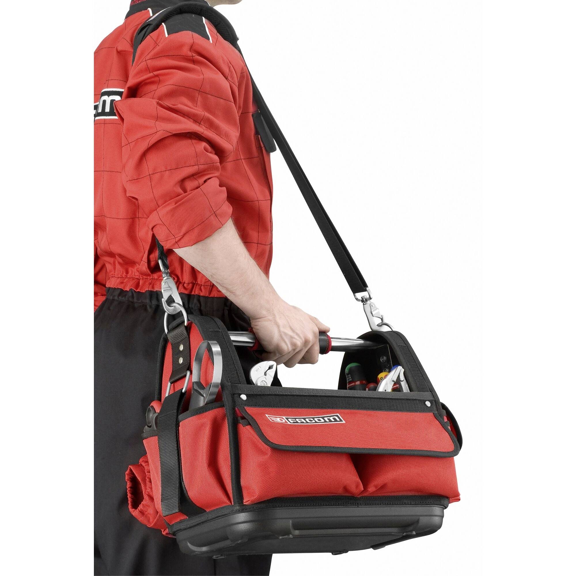 A person wearing a red overall is carrying a red tool bag with a shoulder strap. The bag is partially filled with tools.
