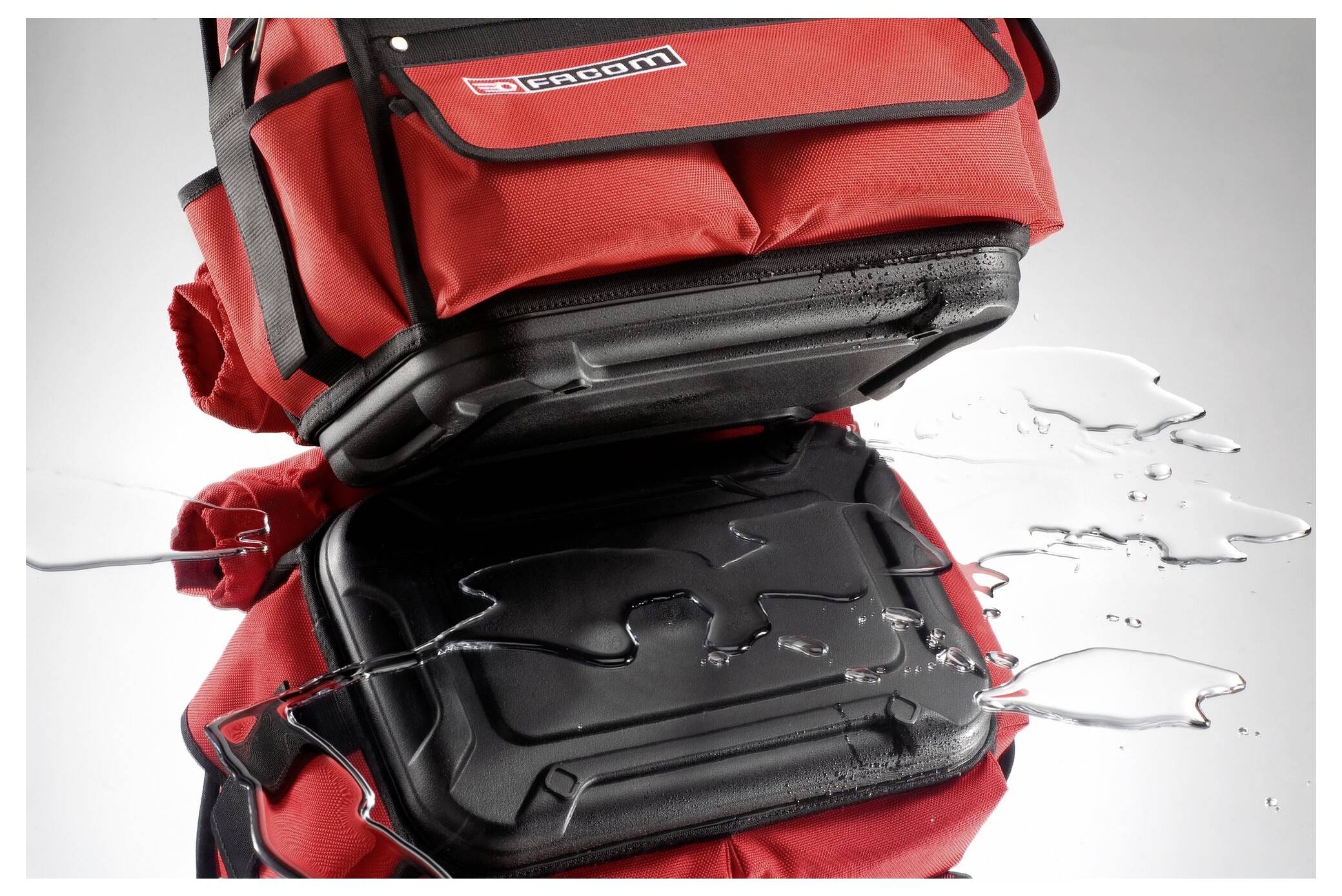 A red rucksack in close-up, its surface water-resistant. Water droplets roll off and do not adhere.