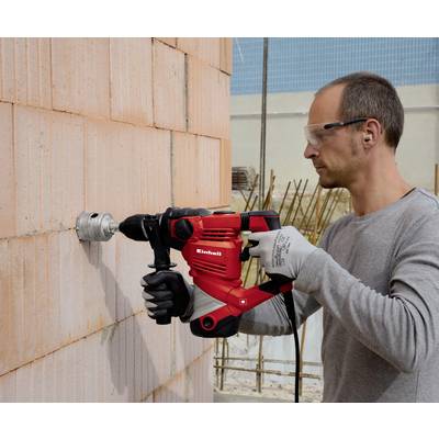 A man wearing safety glasses is using a red drill to bore a hole in a brick wall.