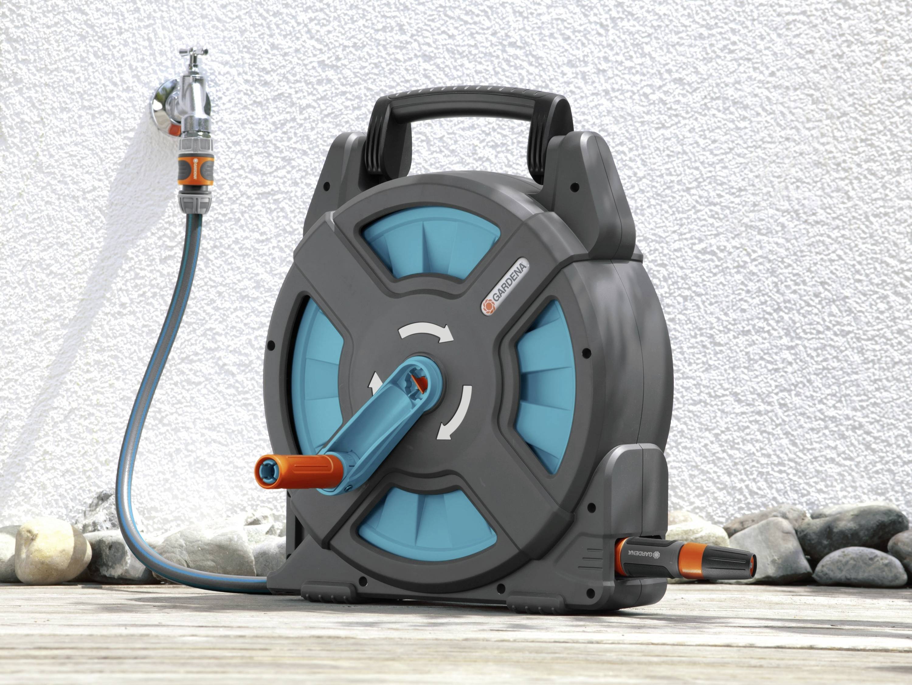 A coiled garden hose in a black casing with blue accents stands on a wooden decking in front of a white wall.