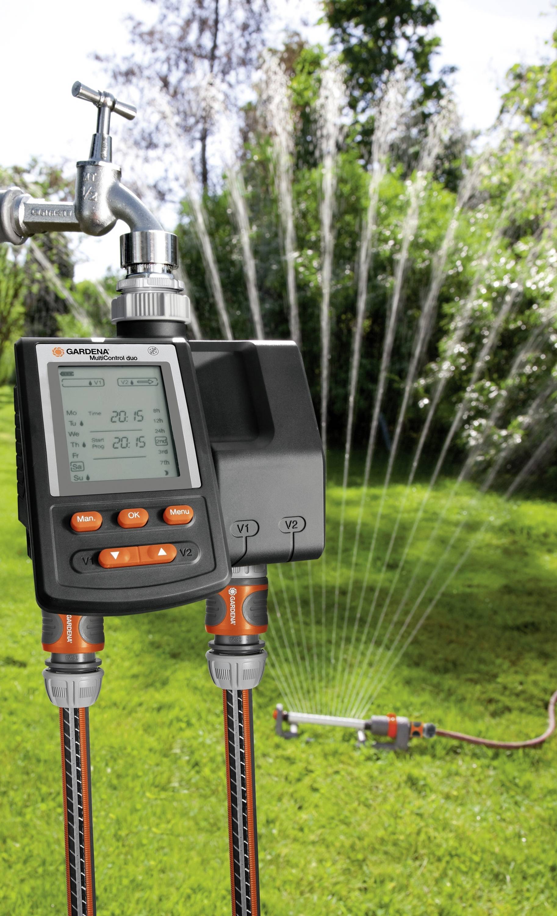 'GARDENA irrigation control' attached to a tap, programmed for automatic garden watering. Lawn with sprinkler in the background.