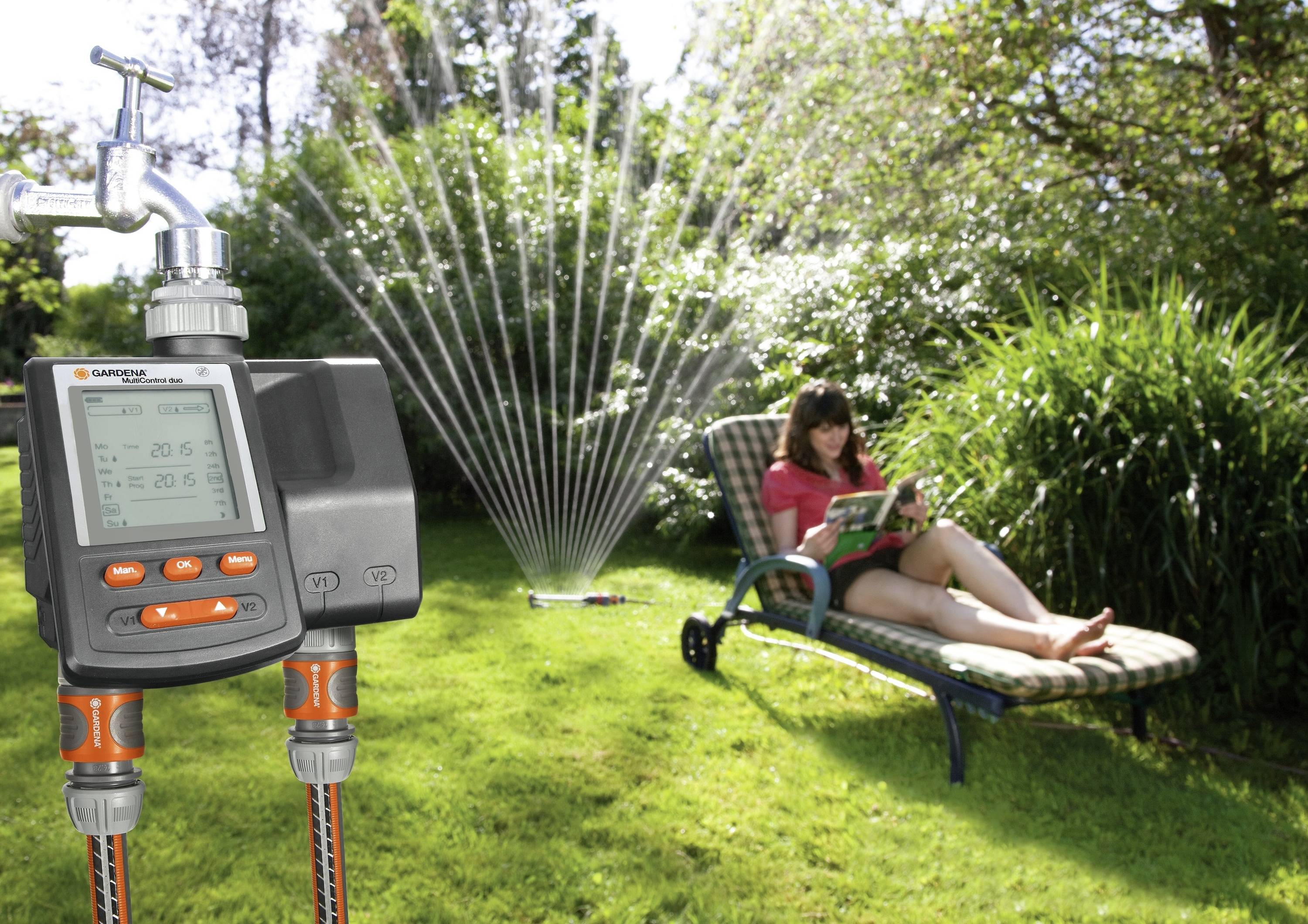 A sprinkler controller operates a lawn sprinkler in the garden. In the background, a person is reading a book while lounging on a deckchair.