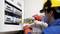 A technician wearing a safety helmet is checking the electrical distribution board with a multimeter.