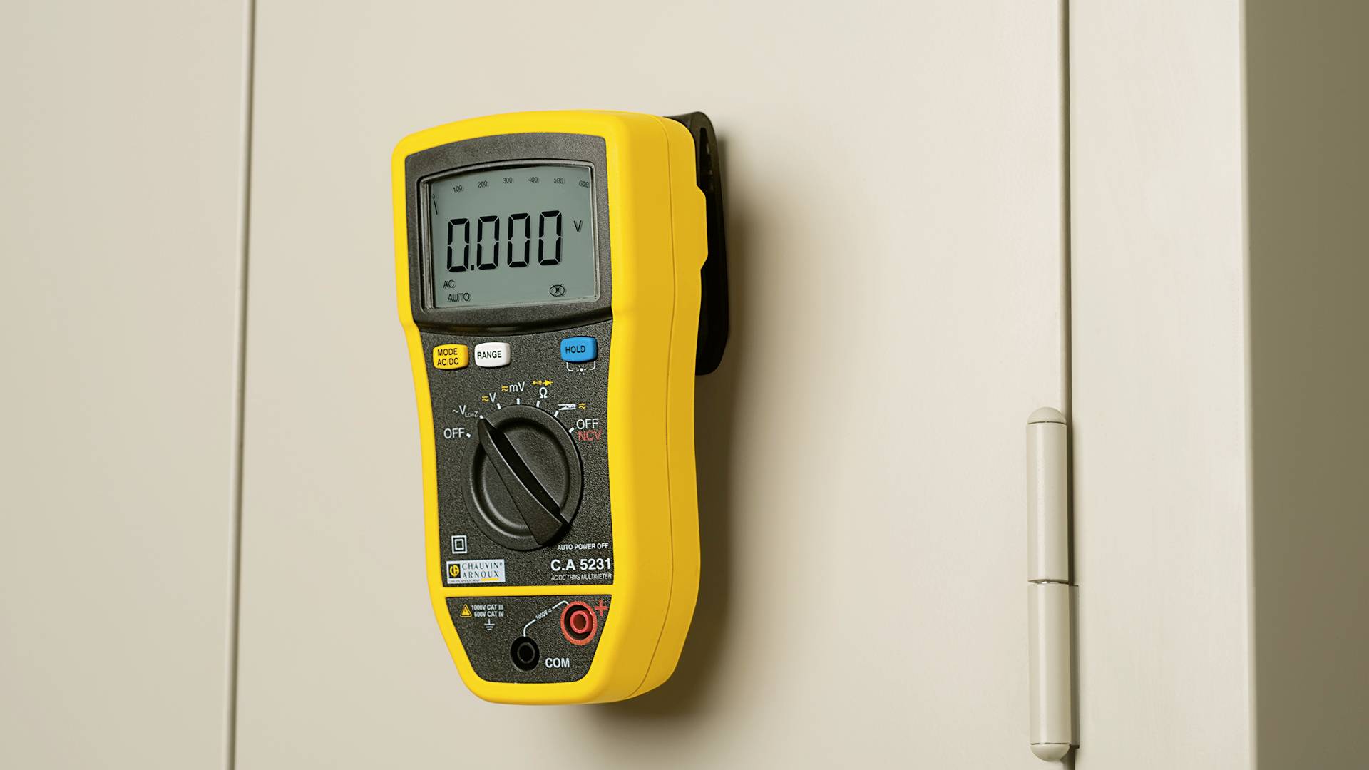 A yellow digital multimeter is attached to a grey cabinet, displaying '0.000 V' on the screen.