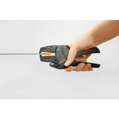 A hand holds wire strippers that are stripping a grey cable. The pliers are black with orange elements, against a grey background.