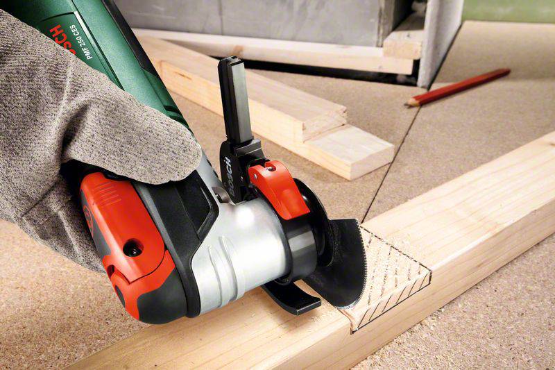 A hand wearing a work glove is holding an electric angle grinder aimed at a piece of wood with marked cutting lines.