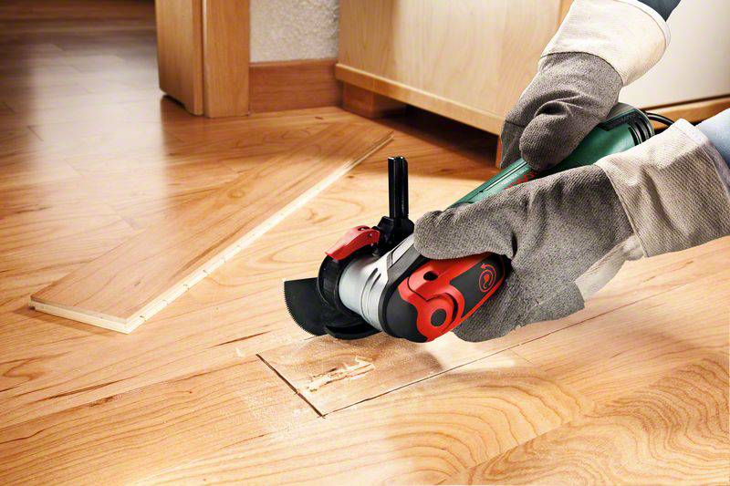 A person is cutting a wooden floor with an electric saw in a living space. Protective gloves are being worn.
