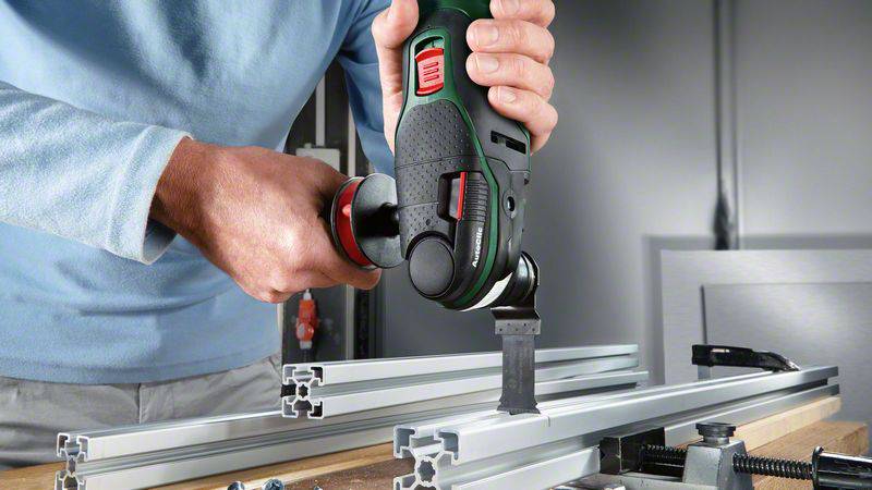 A person is machining an aluminium profile with an electric saw on a workbench in a workshop.