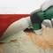 A hand is using an electric tool to remove carpet from a wooden floor. The carpet is partially pulled up.