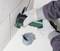 A person is cutting a hole in a white wall using an electric tool. A grey electrical socket is lying nearby.