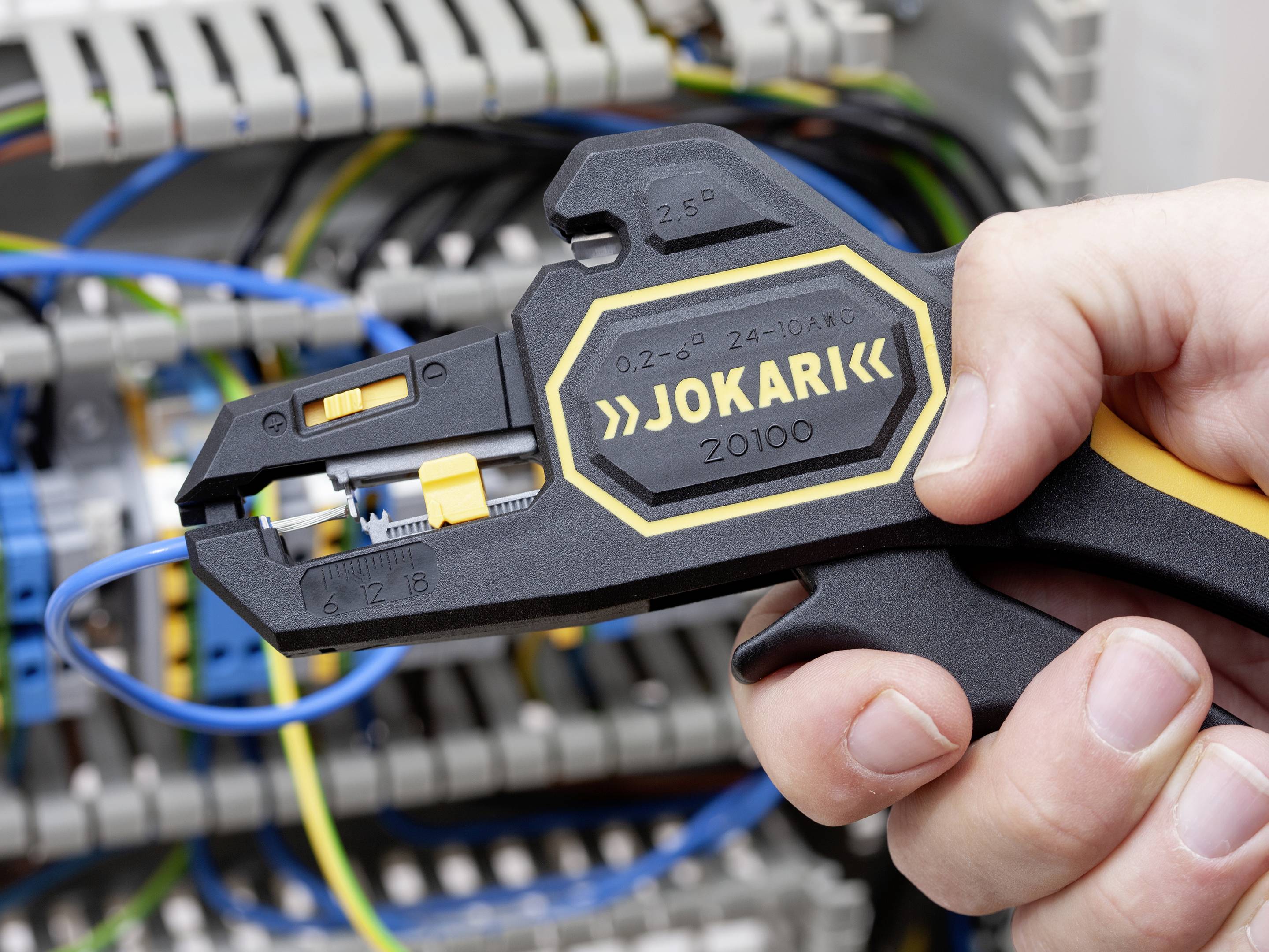 A person is using a wire stripper from the brand 'Jokari' to work on a cable in a switchboard.