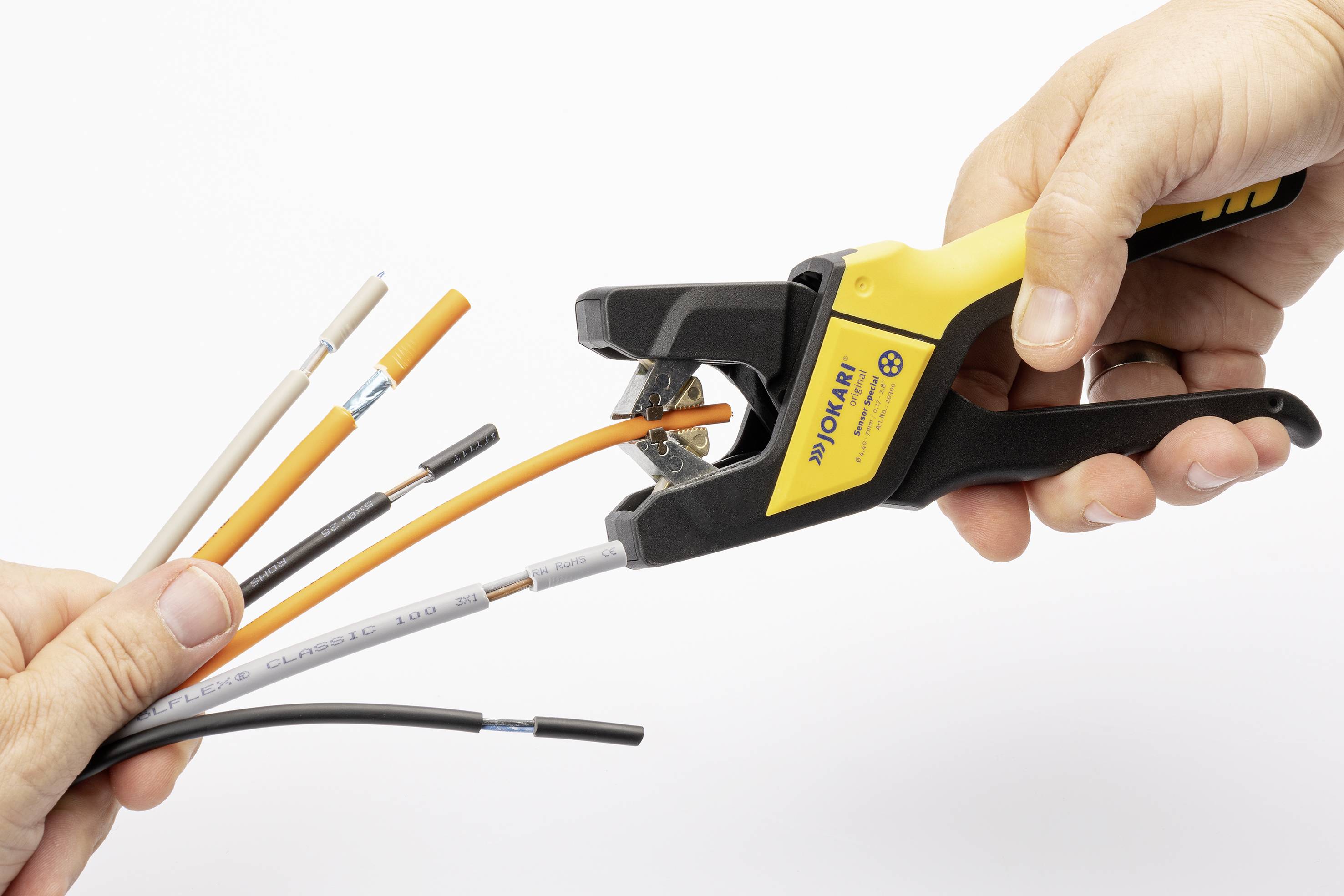 Two hands are holding an automatic wire stripper and cables. One hand is gripping the wire stripper, while the other hand is holding a bundle of cables.