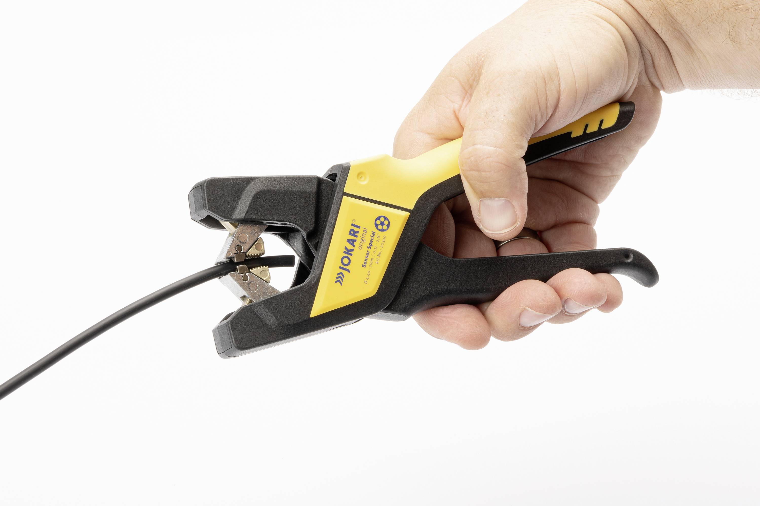 A hand is holding a yellow and black wire stripping pliers by Jokari, which is being used to strip a black cable.