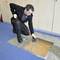 A man in workwear is checking cable bundles underneath a removed floor covering using a specialist tool.