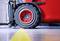 A red forklift is driving over a yellow line on a concrete floor in a warehouse. Only the front wheel is visible.