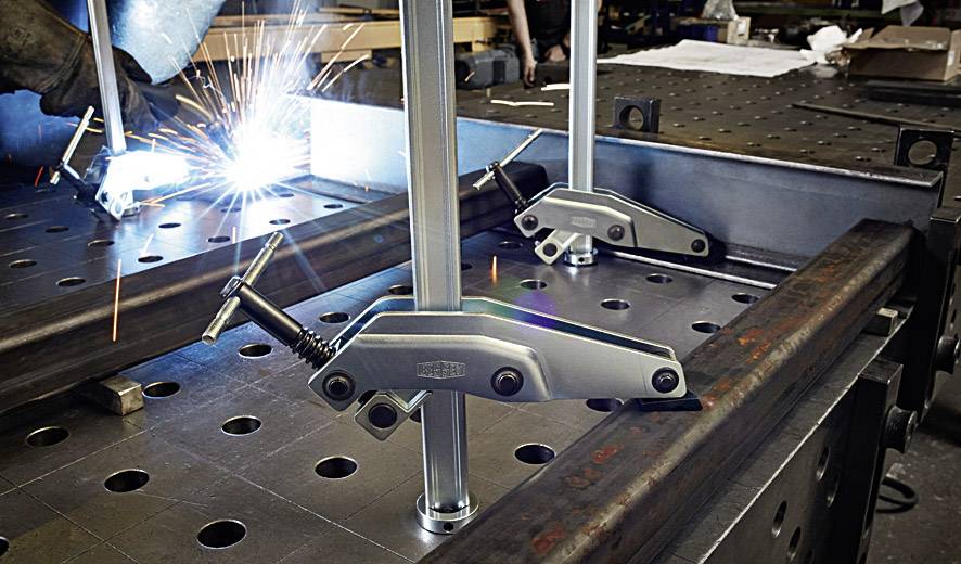 A welding scene in a workshop. Sparks are flying as metal parts are clamped together on a workbench.