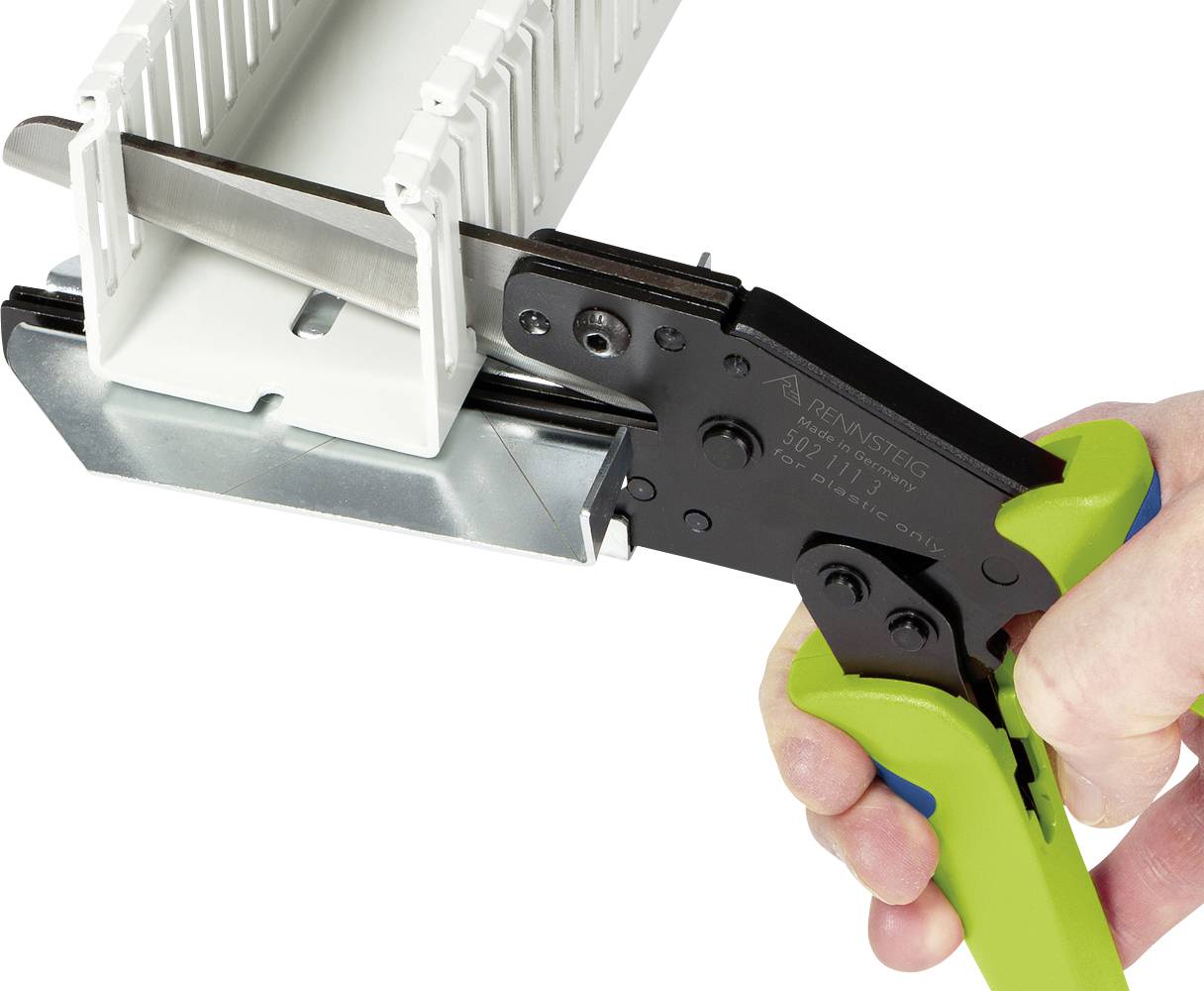 A hand is holding a green pliers, cutting a plastic channel cover along a metal edge in a technical environment.