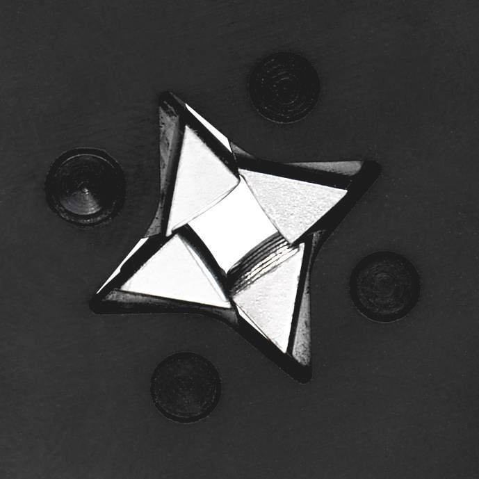 A silver, star-shaped metal object lies on a dark surface, surrounded by several smaller round objects.
