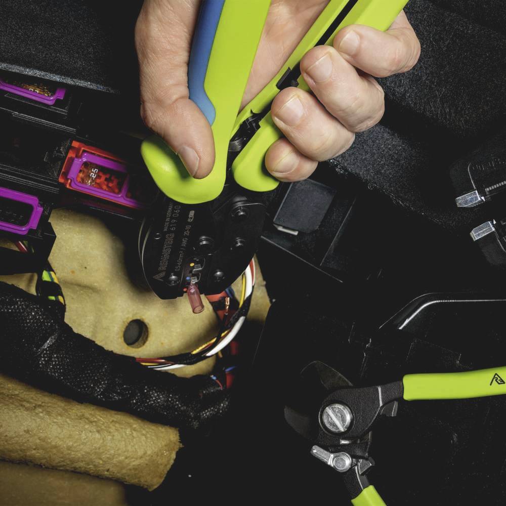 A hand is using a cable cutter with green handles. Electrical wires are visible, extending from a device.