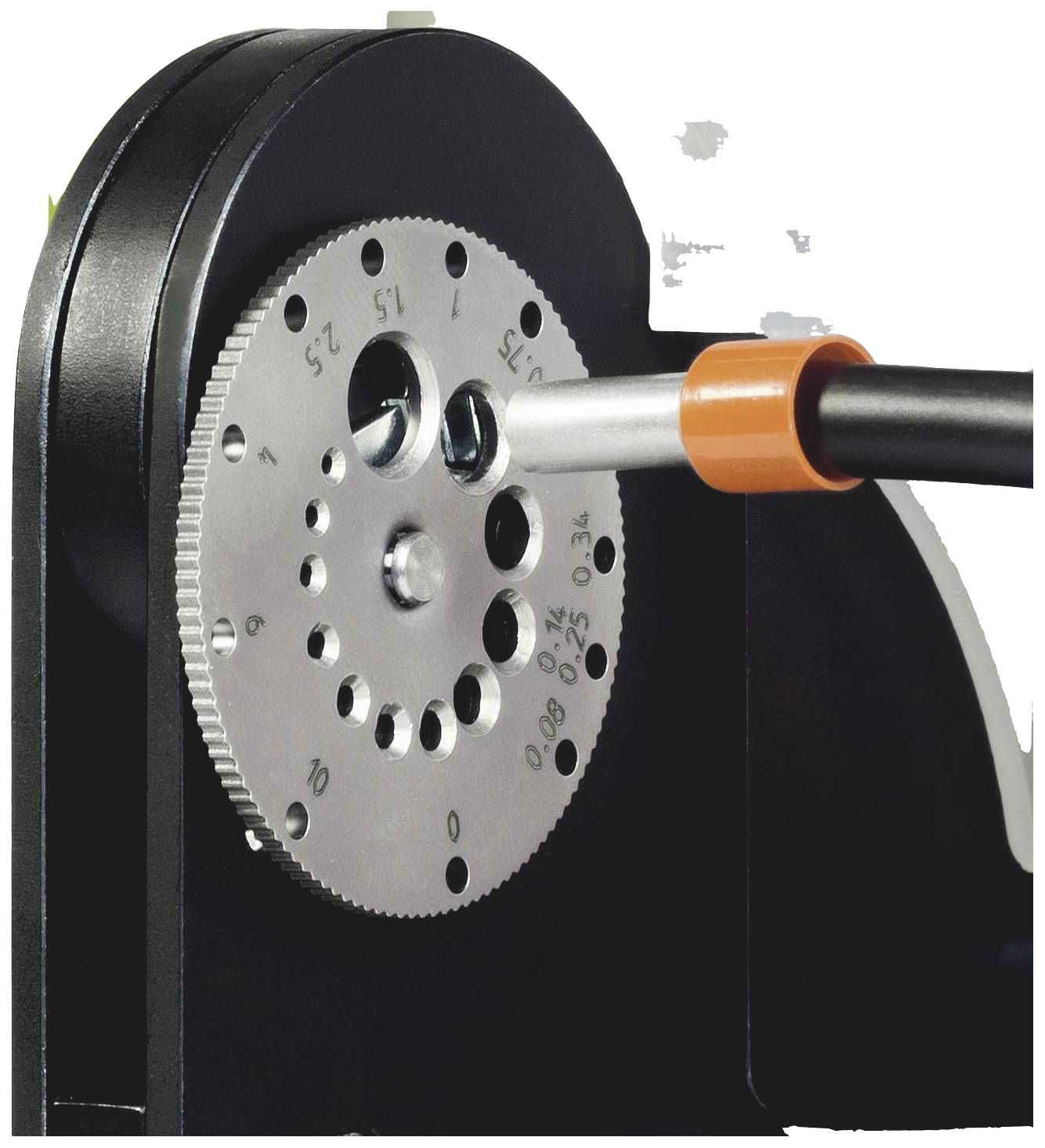A gear wheel with multiple hole sizes on a black metal plate. A cable is being routed through one of the openings.