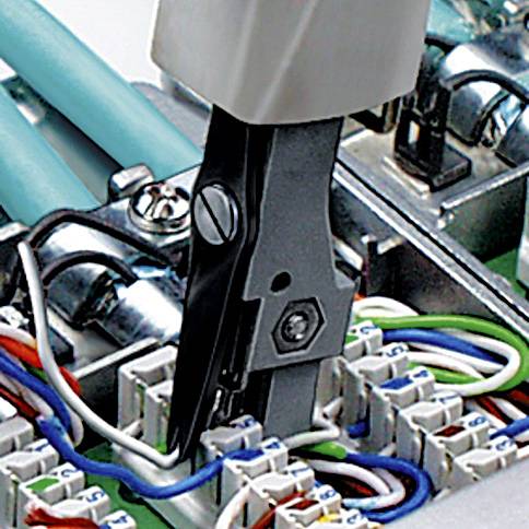 Close-up of pliers working on cables in a distribution box. Cable connections, wire links, and tools are visible in the background.