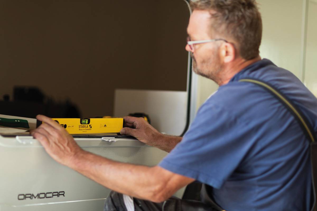 A man is checking the alignment of an object with a spirit level. He is wearing a blue T-shirt and is focused on his work.