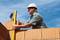 A construction worker wearing a hard hat is aligning brickwork using a spirit level. Clear sky in the background.