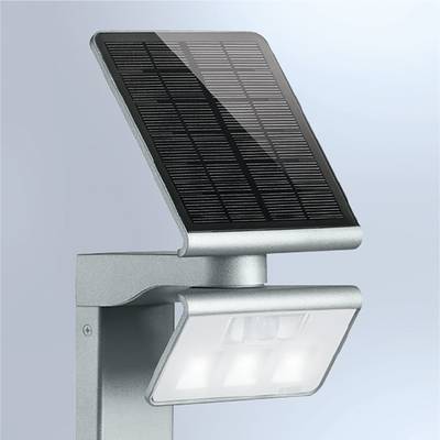A silver, wall-mounted solar lamp with a solar panel on top and three LEDs beneath. It illuminates with bright light.
