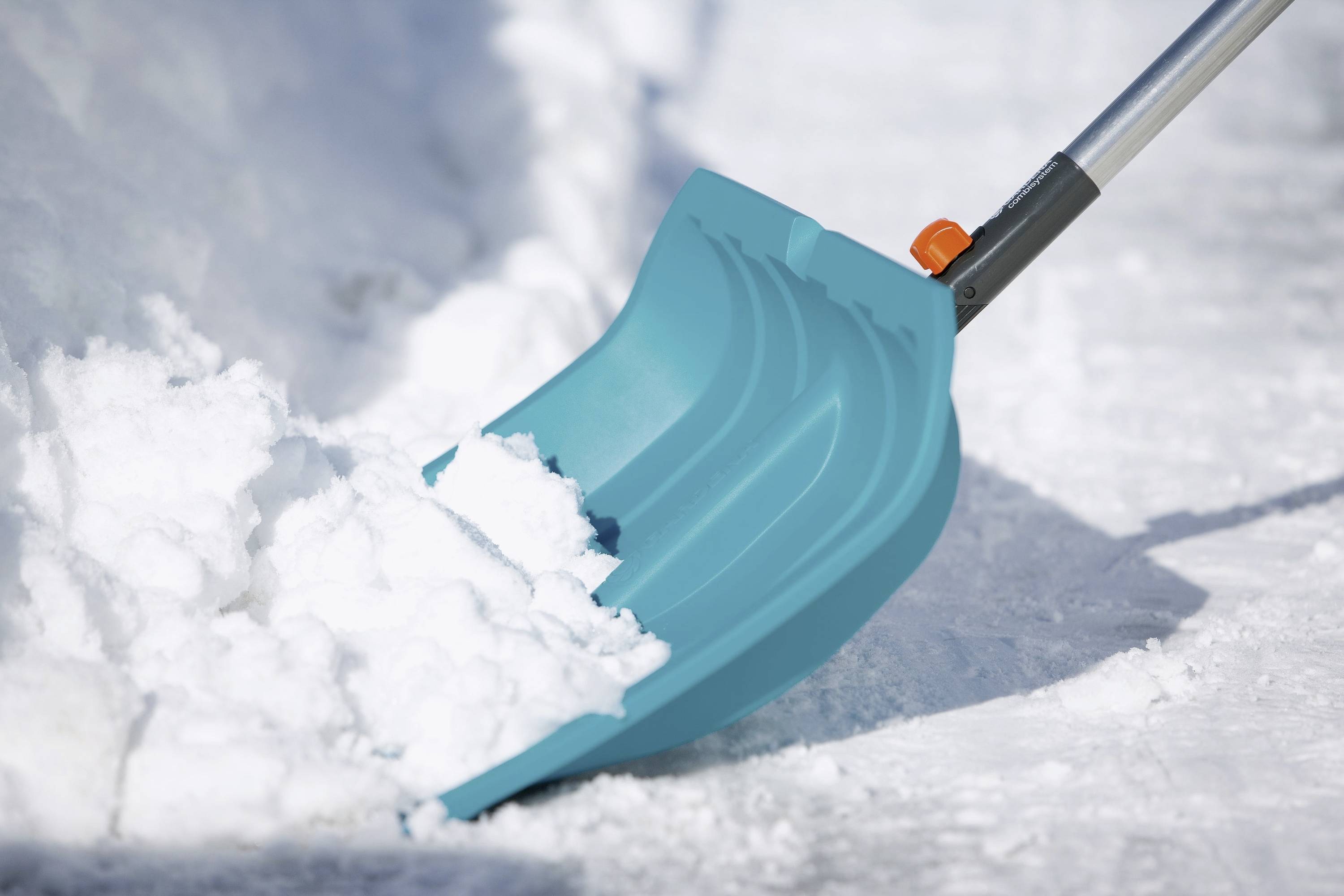 A blue snow shovel moves snow from a pavement. The focus is on the shovel with a background of white snow.