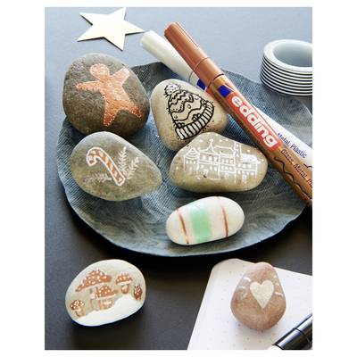 Decorated painted stones and a marker on a plate, featuring holiday-themed drawings like a star, candy cane, house, tree, and heart.