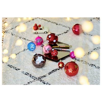 Assorted colorful Christmas ornaments and pens arranged on a smartphone on a patterned surface, with warm bokeh lights in the foreground.