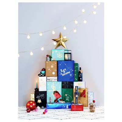 Stack of colorful wrapped Christmas gifts with a gold star on top, set under glowing string lights on a patterned white surface.
