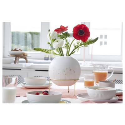 A white vase of red and white flowers centered on a breakfast table set with bowls, glasses, and juice by a bright window.<br>