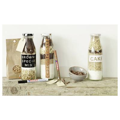 Three homemade dessert mix jars labeled 'BROWNIE SPECIAL MIX', 'CHOCOLATE CAKE', and 'CAKE' on a rustic wooden table, with a paper bag, markers, and a bowl of nuts.