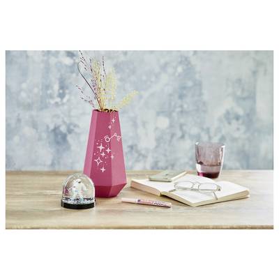 A pink vase with dried flowers sits on a desk beside an open notebook, glasses, pen, phone, and snow globe.<br>