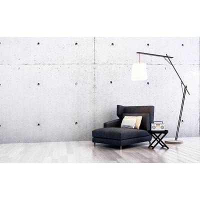 A modern, minimalist space with a grey armchair, a standard lamp, and a small table with a radio in front of a concrete wall.